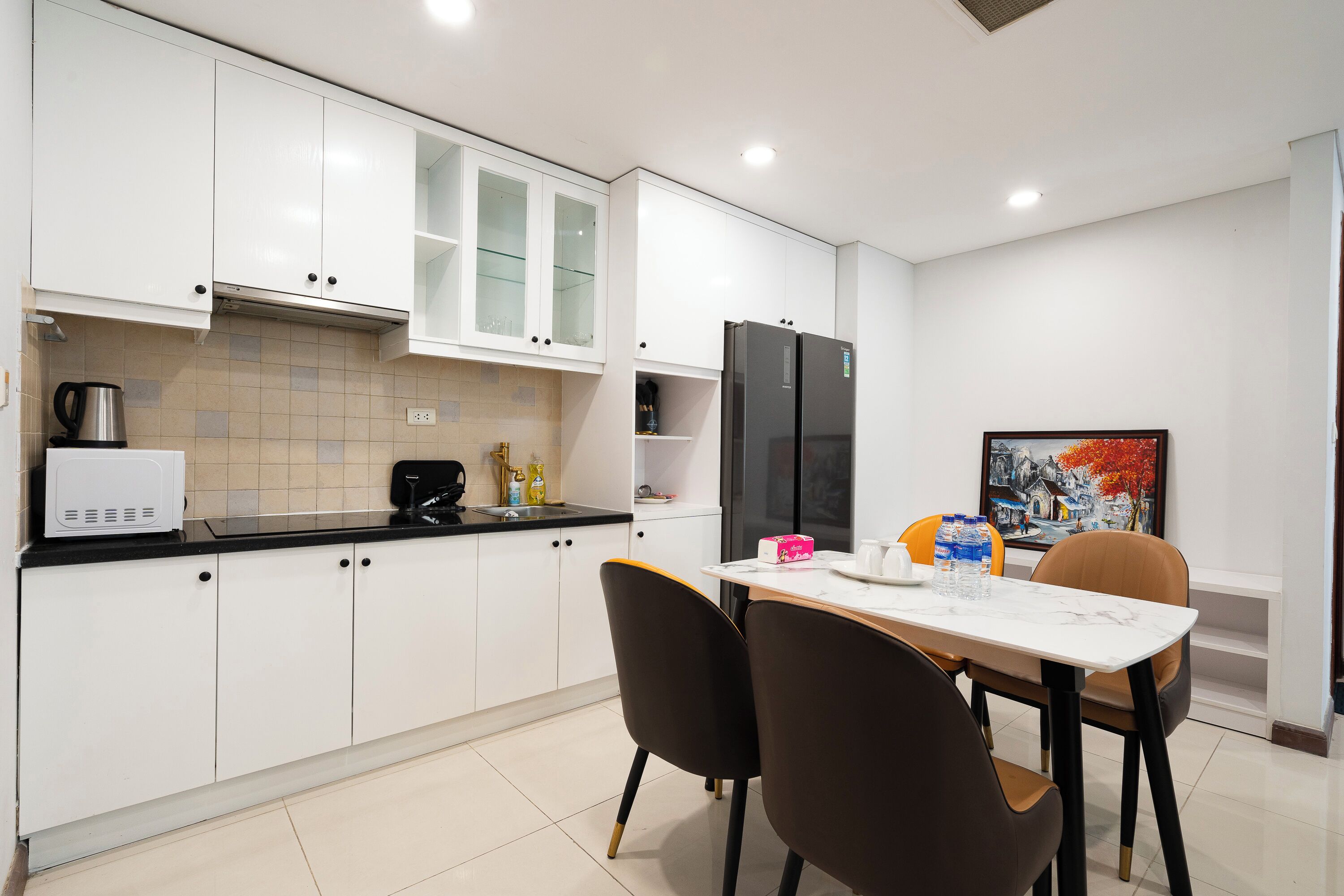 Une cuisine moderne avec des meubles blancs, un réfrigérateur noir et un coin repas comprenant une table et des chaises blanches.