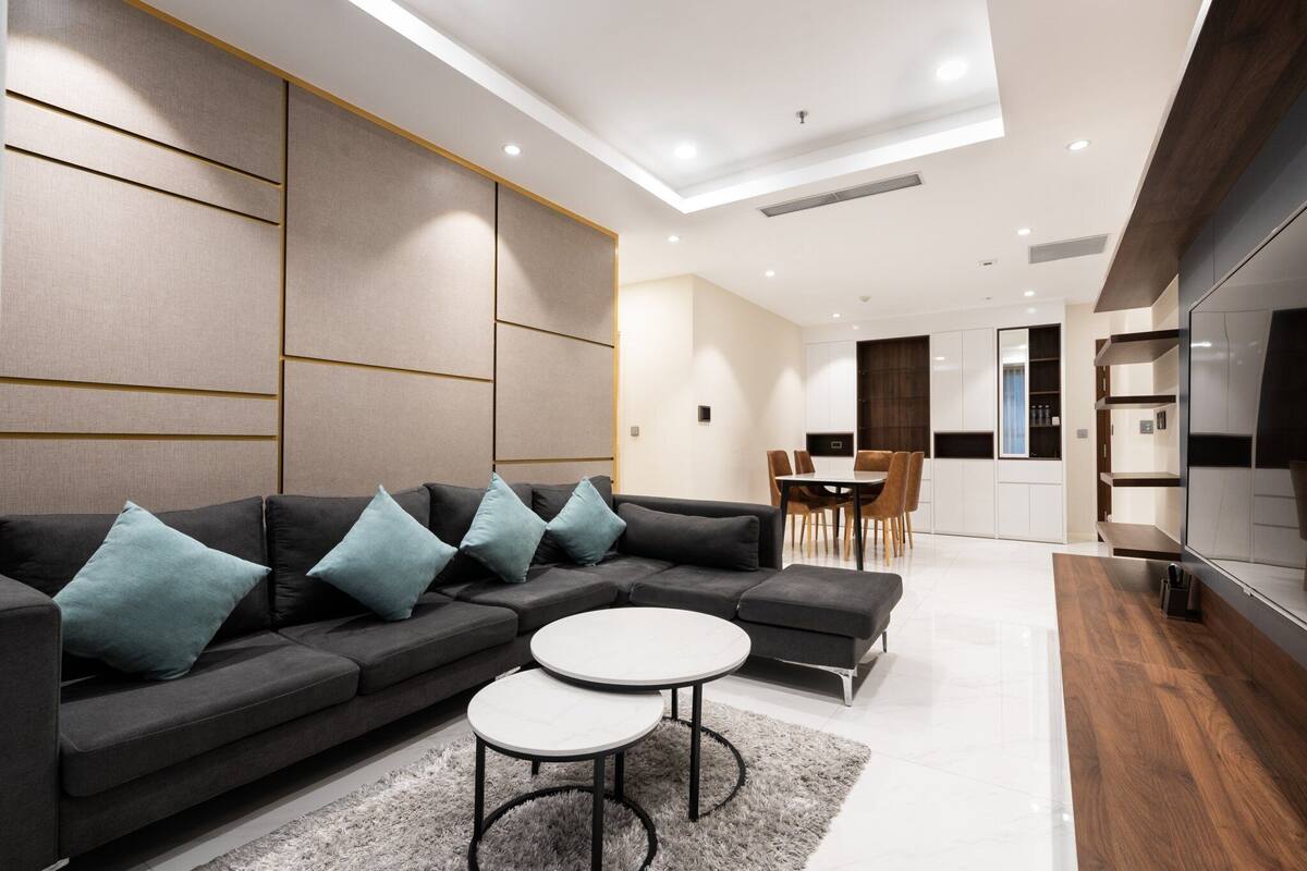 Ein modernes Wohnzimmer mit einem Ecksofa, zwei runden Beistelltischen und einem Essbereich mit Stühlen.