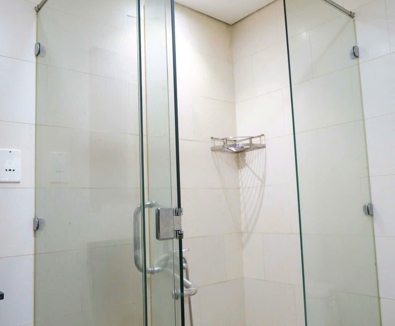 Une douche fermée par des parois en verre, dotée d’une poignée en métal et d’une petite étagère.