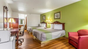 A hotel room with two beds, a desk with a lamp, a red chair, and a television. - Rodeway Inn Santa Rosa, NM (Santa Rosa)
