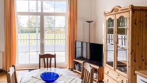 Ein Zimmer mit Esstisch, Stühlen, Fernseher und einem Holzschrank.