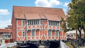 Ein traditionelles Fachwerkhäuschen mit rotem Ziegeldach und einem Kanal davor, sowie eine Fußgängerbrücke.