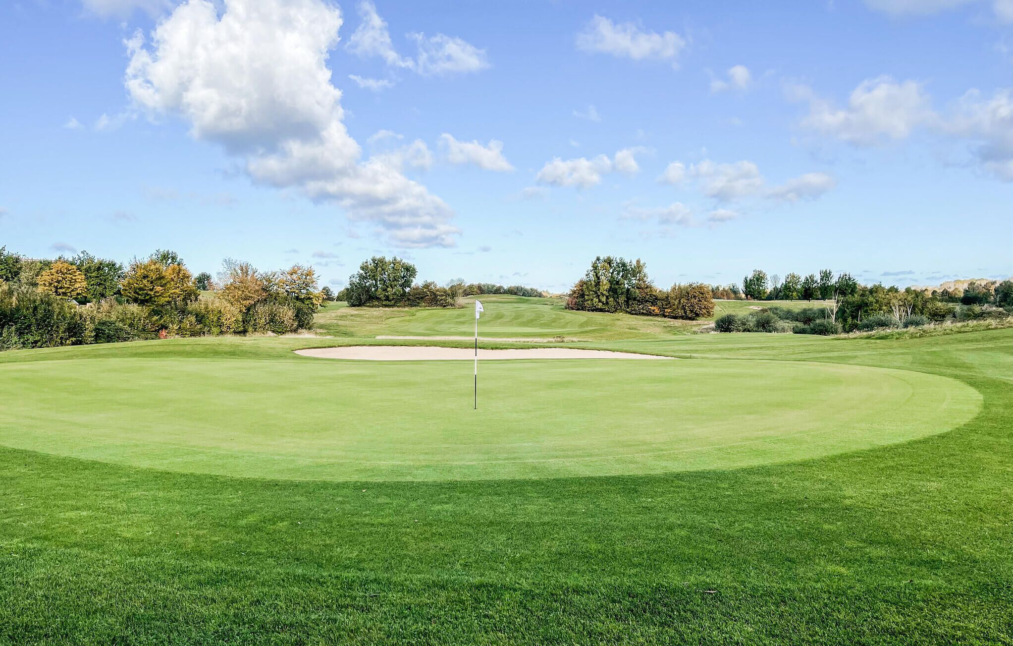 Um campo de golfe com um green bem cuidado, bunkers de areia e uma haste de sinalização.
