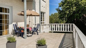 Eine Terrasse im Freien mit Tisch und Stühlen, einem großen Sonnenschirm und Kübelpflanzen.