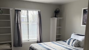 A bedroom with a bed, a ceiling fan, a window with curtains, a white shelving unit, and a carpeted floor. - Charming, Cozy Boise Duplex (Boise)