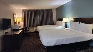 Ein Hotelzimmer mit zwei Betten, einem Schreibtisch mit Computer, einem Fernseher und einem Fenster mit Vorhängen.