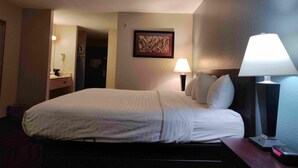 Ein Hotelzimmer mit Bett, Nachttischlampen, einem Nachttisch, einem gerahmten Bild an der Wand und einer Tür zu einem anderen Raum.