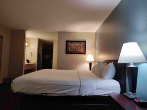 Ein Hotelzimmer mit Bett, Nachttischlampen, einem Nachttisch, einem gerahmten Bild an der Wand und einer Tür zu einem anderen Raum.
