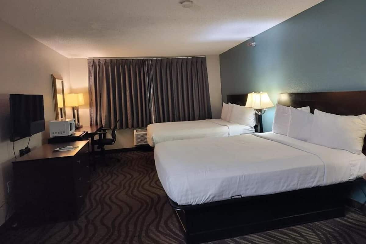 A hotel room with two beds, a desk with a computer, a TV, and a large window with curtains.