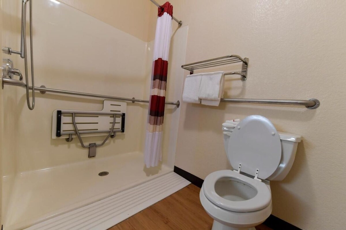 A bathroom with a shower, toilet, grab bars, and a towel rack.