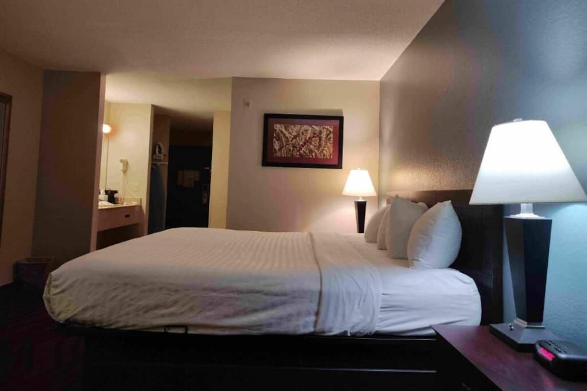 A hotel room with a bed, bedside lamps, a nightstand, and a framed picture on the wall.