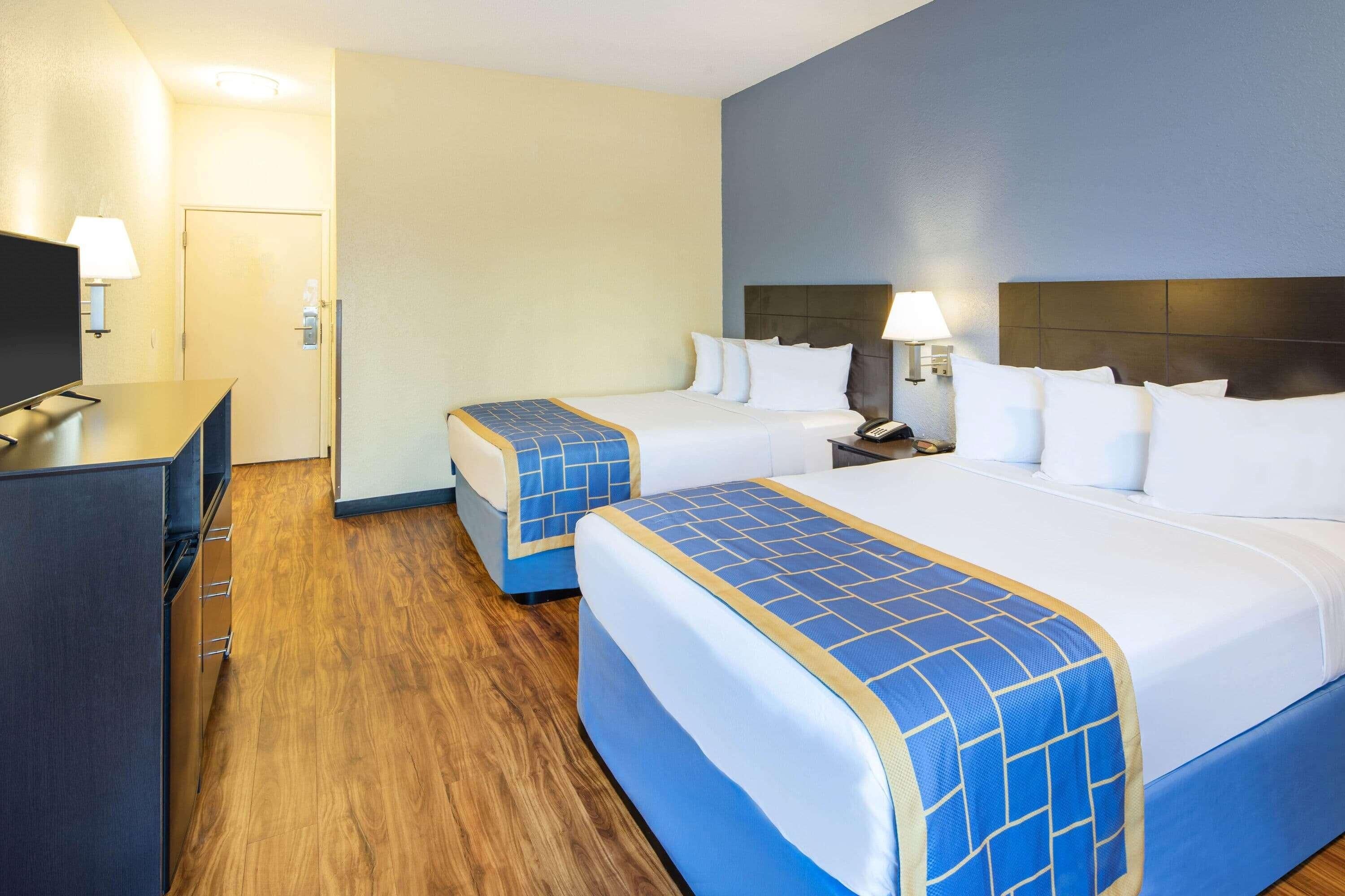 A hotel room with two beds, a TV, a desk, and a lamp.