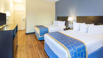 A hotel room with two beds, a TV, a desk, and a lamp.