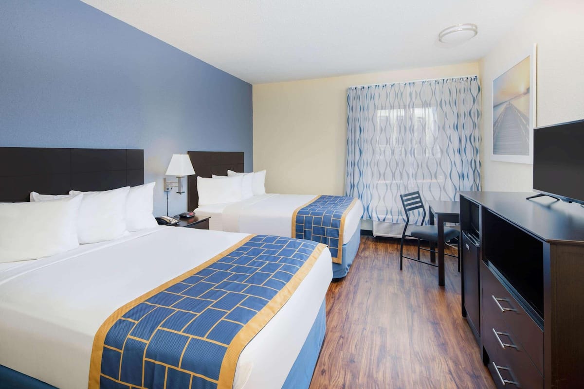 A hotel room with two beds, a desk, a chair, a television, and a window with curtains.