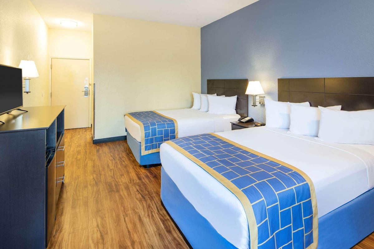 A hotel room with two beds, a TV, a desk, and a lamp.