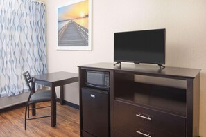 A compact room with a desk, a chair, a microwave, a flat-screen TV, and a framed picture of a pier. - Days Inn by Wyndham Macon I-75 North (Macon)