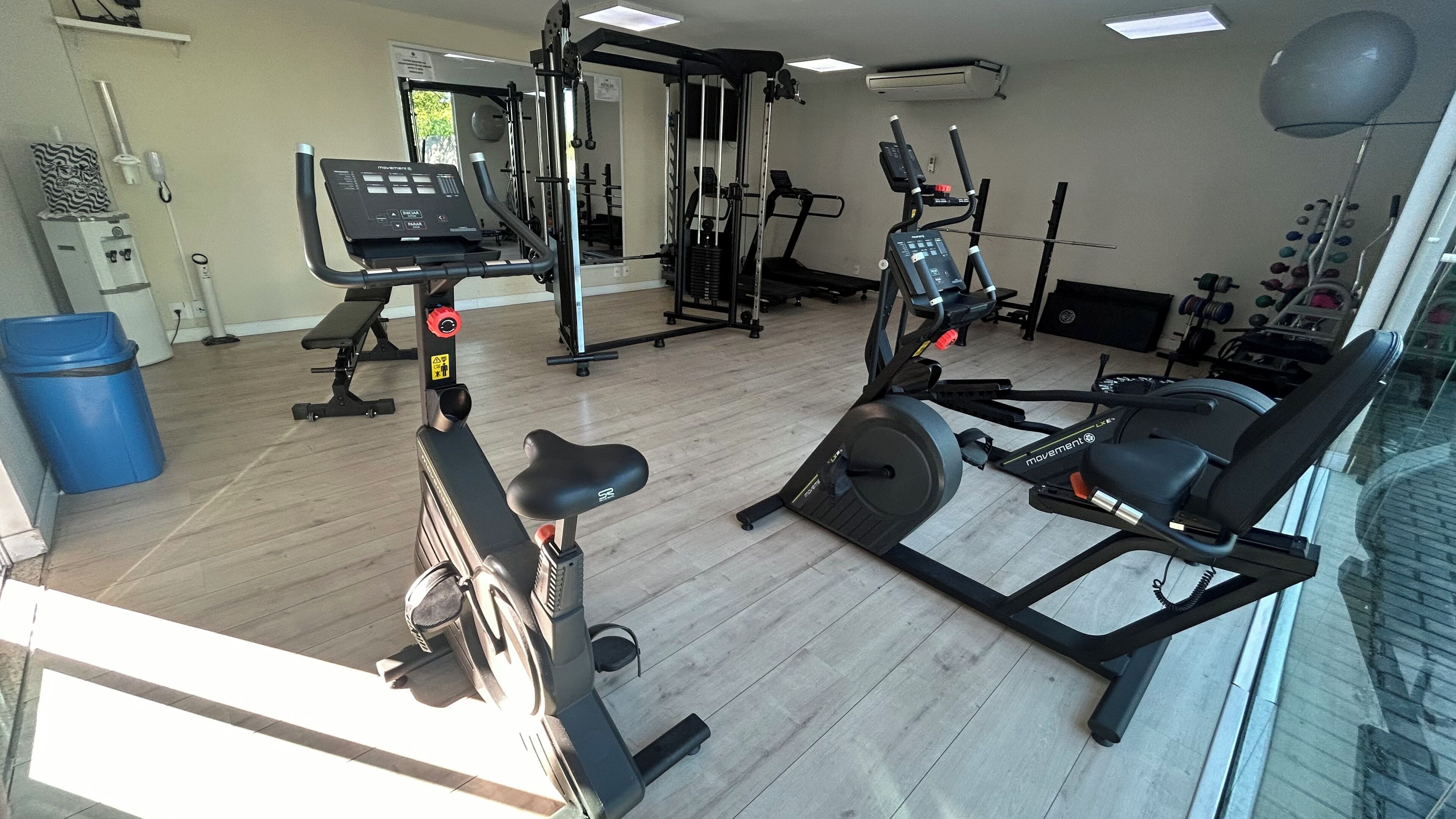 Een fitnessruimte met diverse trainingsapparaten, waaronder een loopband, een hometrainer en krachtapparaten.