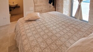 Ein Schlafzimmer mit einer Steinwand, einem Bett mit weißer Spitze, einem Kleiderständer und einem Fenster mit Vorhängen.
