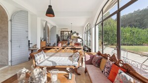 A spacious room with a large window, a wooden sofa, and a table with decorative items. - Centre Ville à Pied Dans une Authentique Bastide Xviieme Rénovée (Aix en Provence)