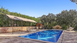 A rectangular swimming pool with a tiled deck, surrounded by trees and a covered seating area with chairs. - Centre Ville à Pied Dans une Authentique Bastide Xviieme Rénovée (Aix en Provence)