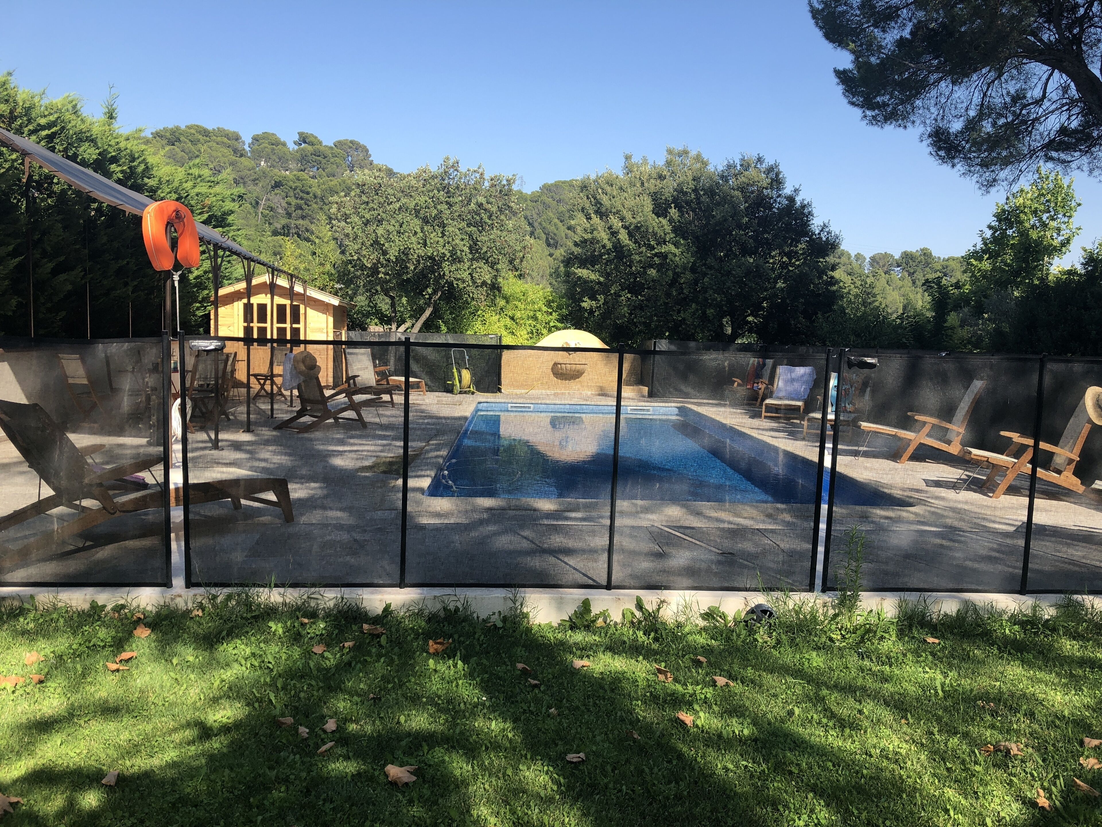 A backyard with a swimming pool, surrounded by a fence, and a yellow building in the background.