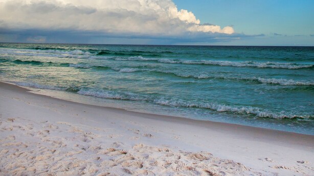 Ein Strand mit Regenbogen, Wellen und einem bewölkten Himmel.