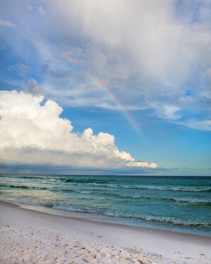 A beach with a rainbow, waves, and a cloudy sky.