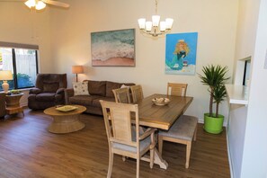 Uma sala de jantar com mesa e cadeiras de madeira, uma mesa de centro redonda e um vaso de planta.