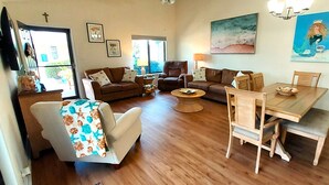 Ein Wohnzimmer mit einer Couch, Sesseln, einem Couchtisch, einem Esstisch mit Stühlen, einer Lampe und einer Topfpflanze.