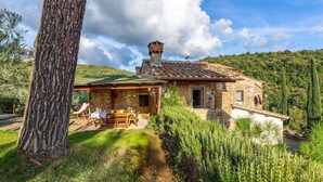 Una casa in pietra con tetto verde, un piccolo portico e un'area pranzo con mobili da esterno.