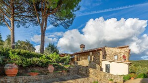 Una casa di pietra rustica con una scala in pietra che conduce a una porta, immersa nel verde e sotto un cielo sereno.
