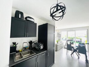 Enjoy cooking in this kitchen with a stainless steel sink, coffee machine, and wine cooler, opening up to a dining area with a large window and outdoor view.