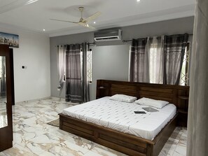 A bedroom with a wooden bed, marble flooring, a ceiling fan, and an air conditioning unit.