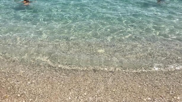 Uma praia com águas claras e rasas e um areal pedregoso.