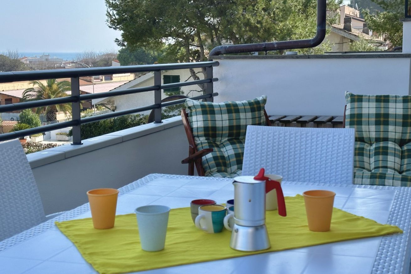 A balcony with a table set for two, featuring a metal coffee pot, two cups, and a yellow placemat.