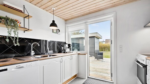 Una cocina moderna con armarios blancos, salpicadero negro y techo de madera.