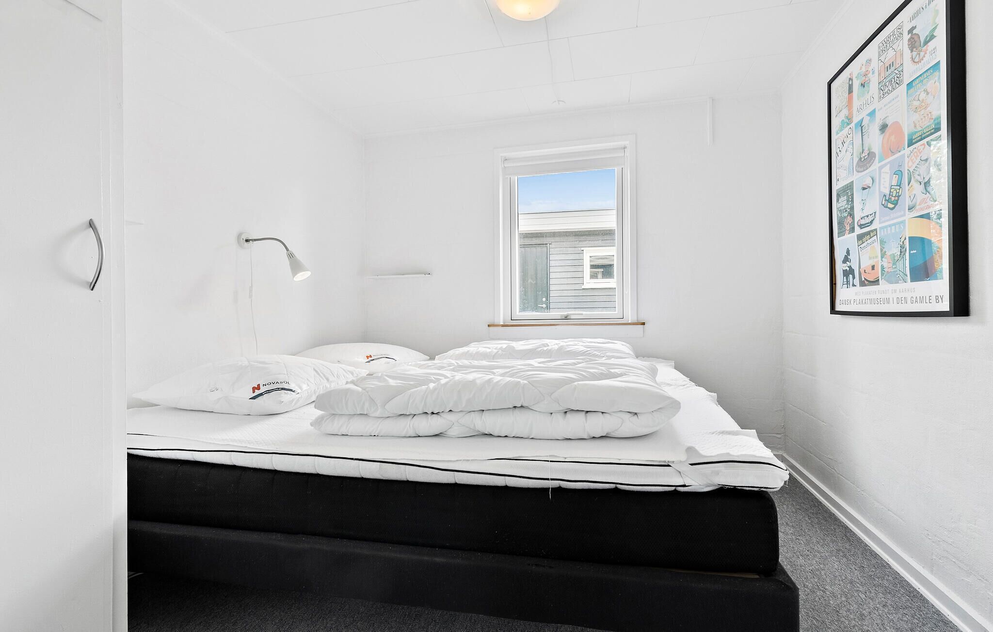 A minimalist bedroom with a bed, a bedside lamp, a window, and a framed picture on the wall.