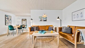 Una sala de estar moderna con piso de madera, un sofá de cuero marrón, una mesa de centro de madera y un comedor con una mesa de madera y sillas verdes.