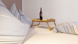 A bed with patterned pillows, a wooden side table with a bottle and glasses, and a plain wall. - Haus Oselbach- Gemütlich, Zentral, Modern (Zweibrücken)