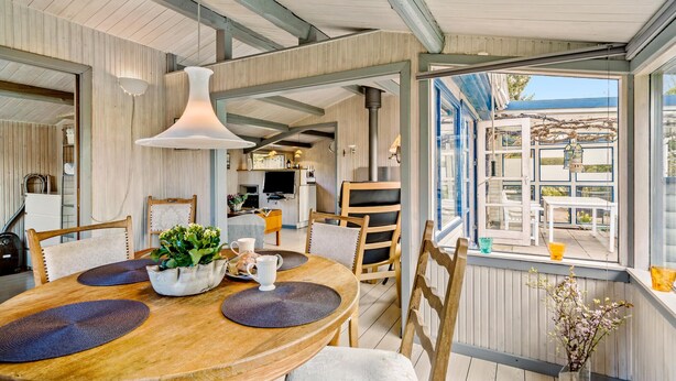 Un coin repas chaleureux avec une table en bois, des chaises et une grande fenêtre donnant sur une terrasse.