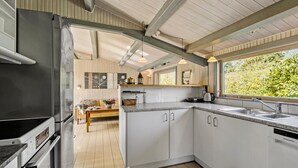 Une cuisine moderne avec des meubles blancs, un four encastré et une grande fenêtre offrant une vue sur la verdure environnante.