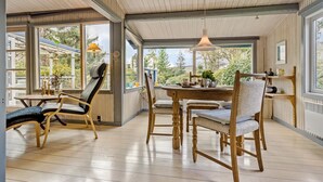 Une pièce spacieuse avec un plancher en bois, une table de salle à manger ronde et deux chaises. De grandes fenêtres offrent une vue sur l’extérieur.