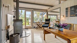 Un intérieur chaleureux avec une table en bois, un fauteuil en cuir et une grande fenêtre donnant sur l’extérieur.