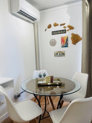 A modern room with a glass table, white chairs, and a wall decorated with Hawaii-themed items. - Parking Included Upgraded w King Bed Marine Surf Waikiki (Honolulu)