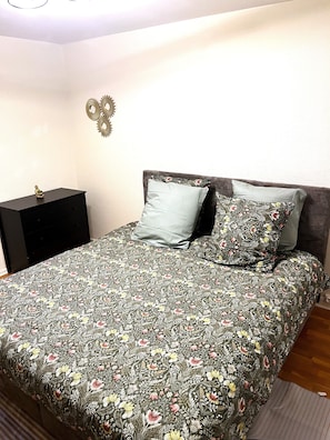 Camera da letto con copriletto a motivi floreali, una testiera in legno scuro e un comodino con un oggetto decorativo.