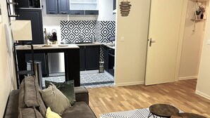 A living room with a sofa, a coffee table, and a rug. There is a kitchen area with cabinets and a microwave. - Charmant Appartement à Metz - Proximité Gare (Metz)