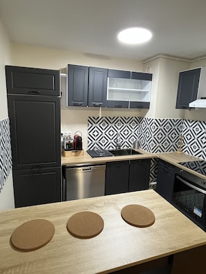 Una cucina moderna con mobili neri, una lavastoviglie in acciaio inox, uno schienale decorato con motivi bianchi e neri e un piano di lavoro in legno con tappetini di sughero.