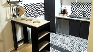 A compact kitchen with a black and white patterned backsplash, a black refrigerator, and a wooden table with a hanging rack. - Charmant Appartement à Metz - Proximité Gare (Metz)