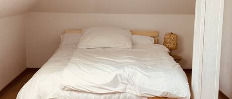 A single bed with a wooden frame and white bedding in a room with wooden flooring and a sloped ceiling.
