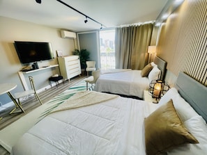 A hotel room with two beds, a TV, a desk, a chair, and a view of the city.